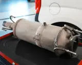 Filtr DPF leżący na czerwonej skrzynce narzędziowej, obok białego samochodu.
