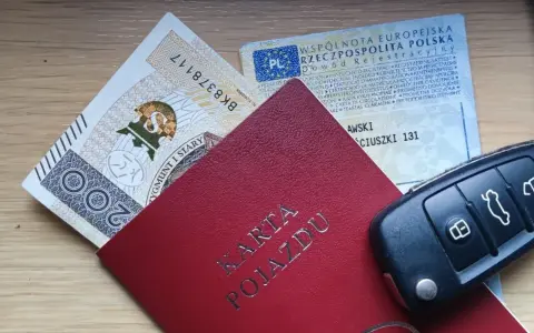 Karta pojazdu, dowód rejestracyjny, pieniądze i kluczyki samochodowe na drewnianym tle.