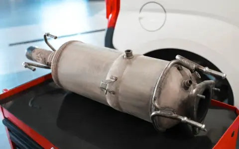 Filtr DPF leżący na czerwonej skrzynce narzędziowej, obok białego samochodu.