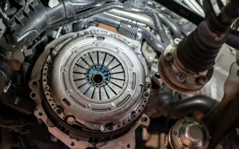 Zbliżenie na mechanizm sprzęgła samochodowego z widocznymi elementami silnika.