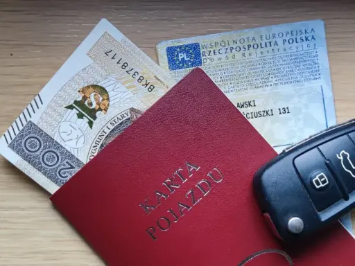 Karta pojazdu, dowód rejestracyjny, pieniądze i kluczyki samochodowe na drewnianym tle.