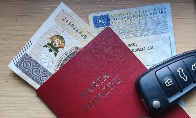 Karta pojazdu, dowód rejestracyjny, pieniądze i kluczyki samochodowe na drewnianym tle.