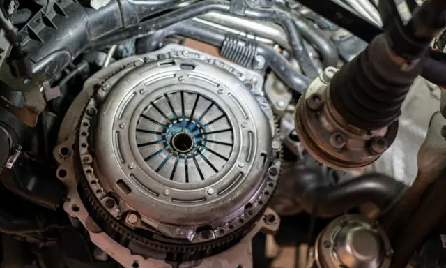 Zbliżenie na mechanizm sprzęgła samochodowego z widocznymi elementami silnika.