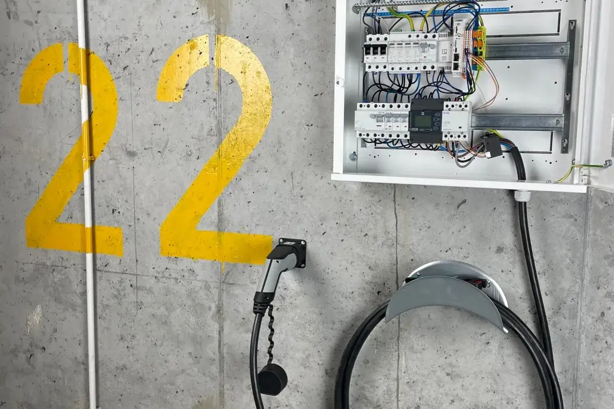 Rodzina ładująca samoch&oacute;d elektryczny w garażu wallboxem, uśmiechnięta, nowoczesny dom